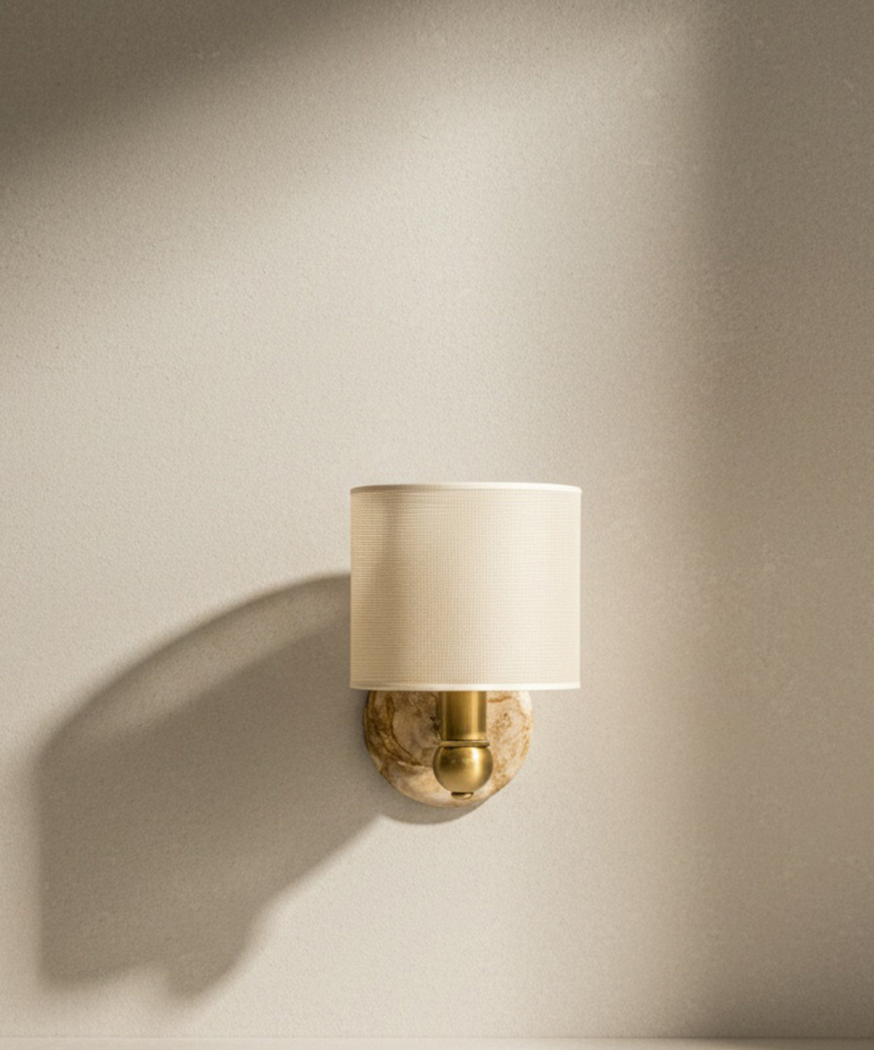 Aplique de pared de lujo con base redonda de mármol veteado, brazo de latón dorado y pantalla de lino color crema sobre fondo neutro.