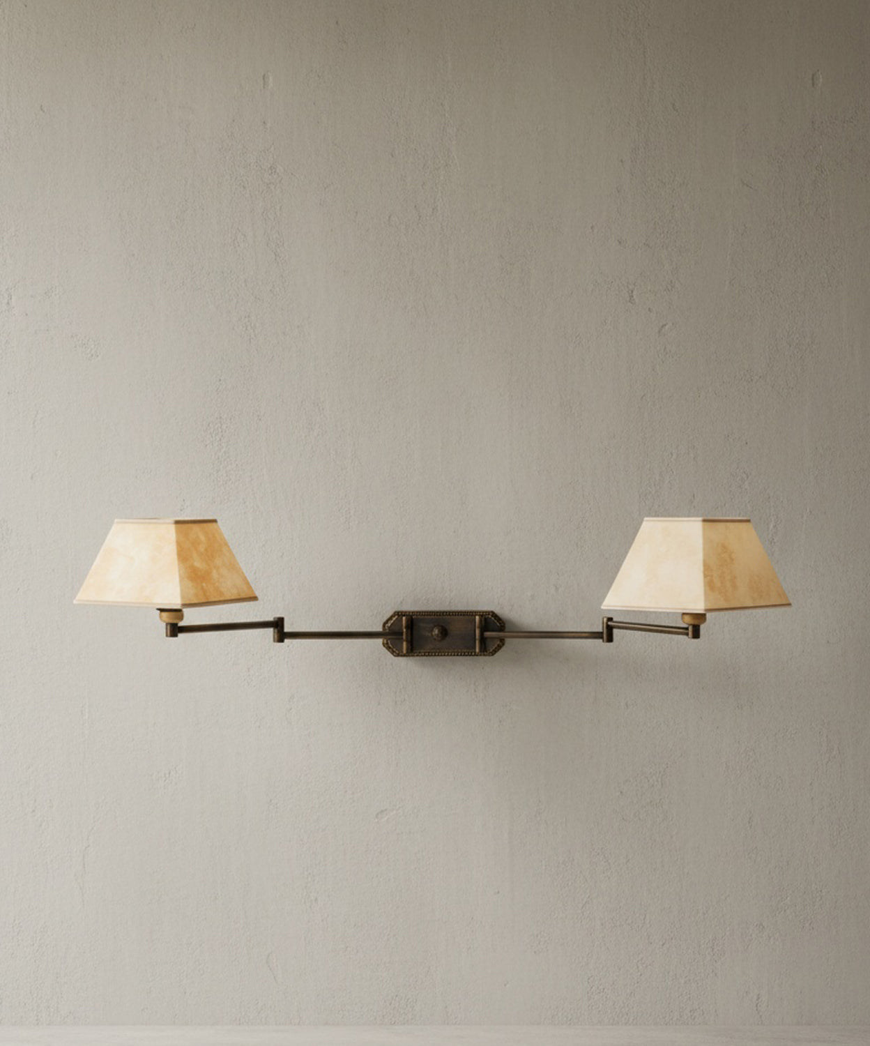 Aplique de pared doble de latón envejecido con brazos articulados y pantallas color crema sobre fondo de cemento pulido.