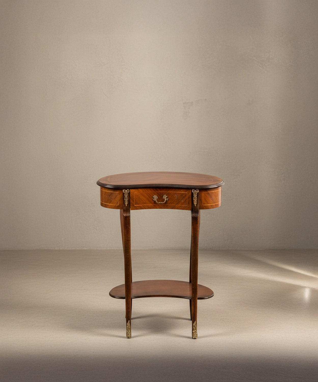 Vista frontal de mesa estilo Luis XV con bronces dorados y cajón central sobre fondo neutro.