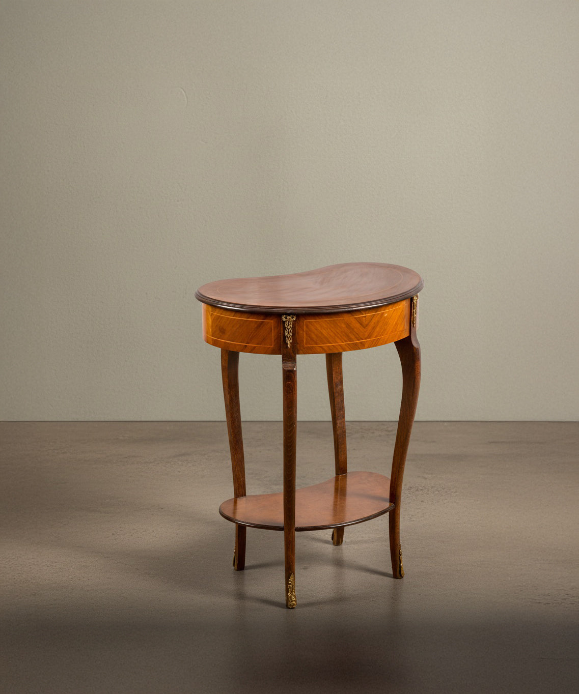 Vista trasera de mesa estilo Luis XV con bronces dorados y cajón central sobre fondo neutro.