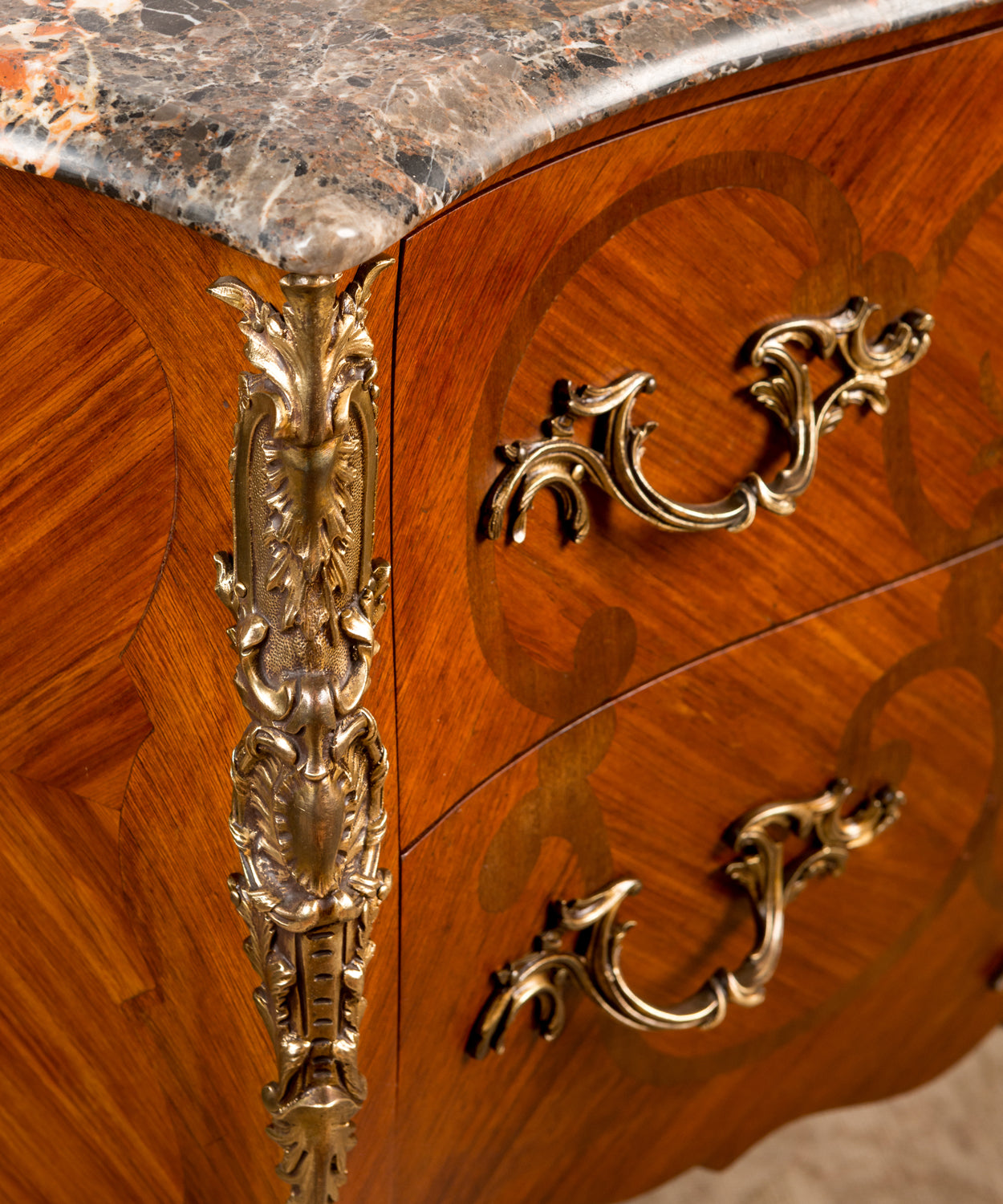 Primer plano de los herrajes de bronce dorado y el canto moldurado del mármol veteado.