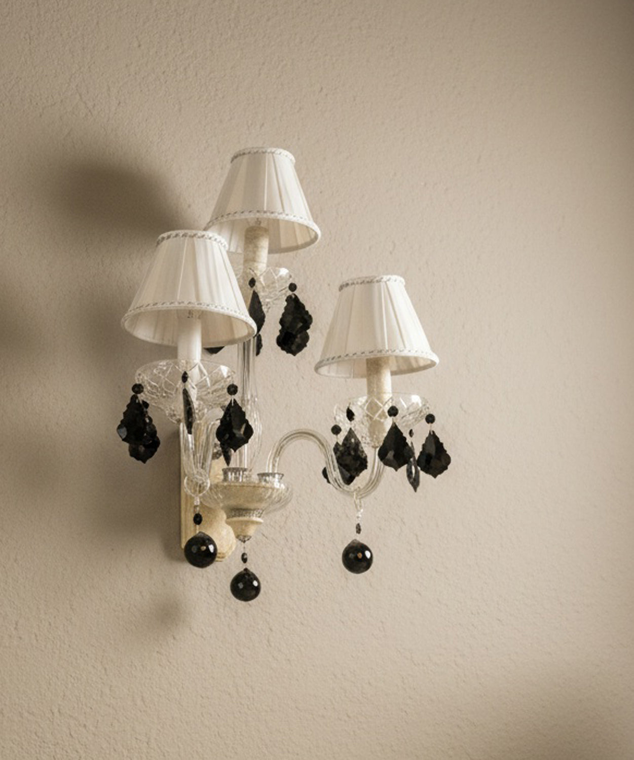 vista lateral Aplique de pared vintage de 3 luces con brazos de cristal y lágrimas negras colgantes sobre pared beige.