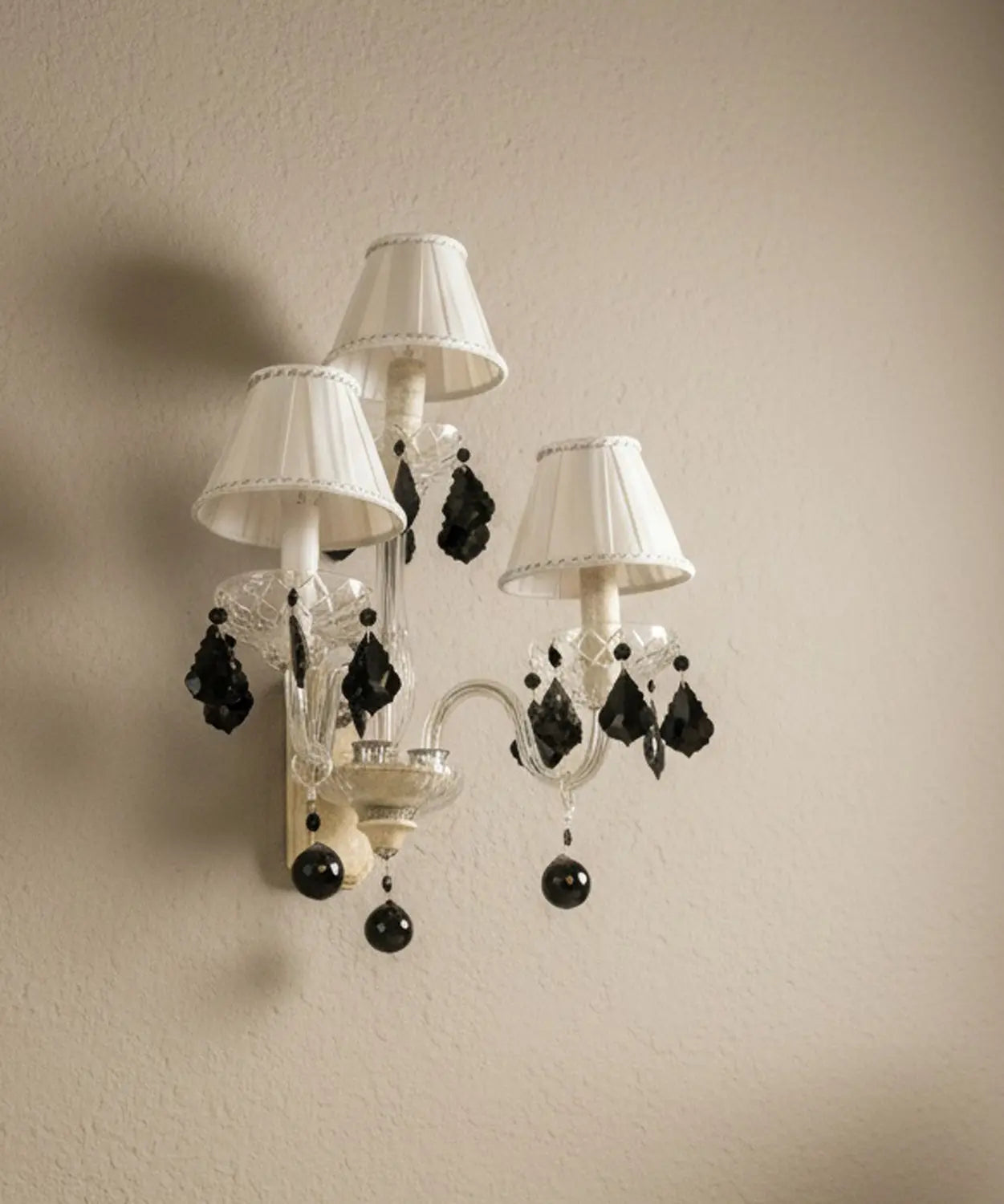 vista lateral Aplique de pared vintage de 3 luces con brazos de cristal y lágrimas negras colgantes sobre pared beige.