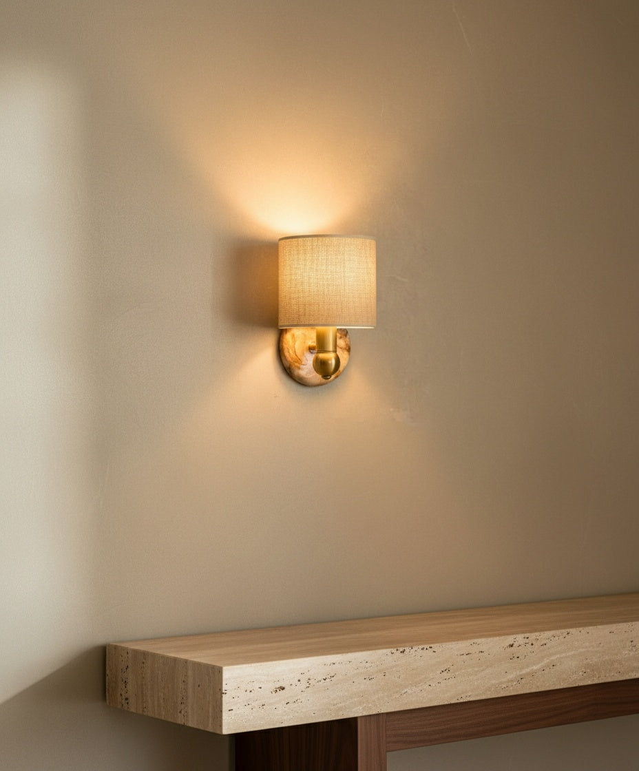 El aplique iluminado sobre una consola de travertino, proyectando una luz cálida y sombras suaves en forma de abanico.