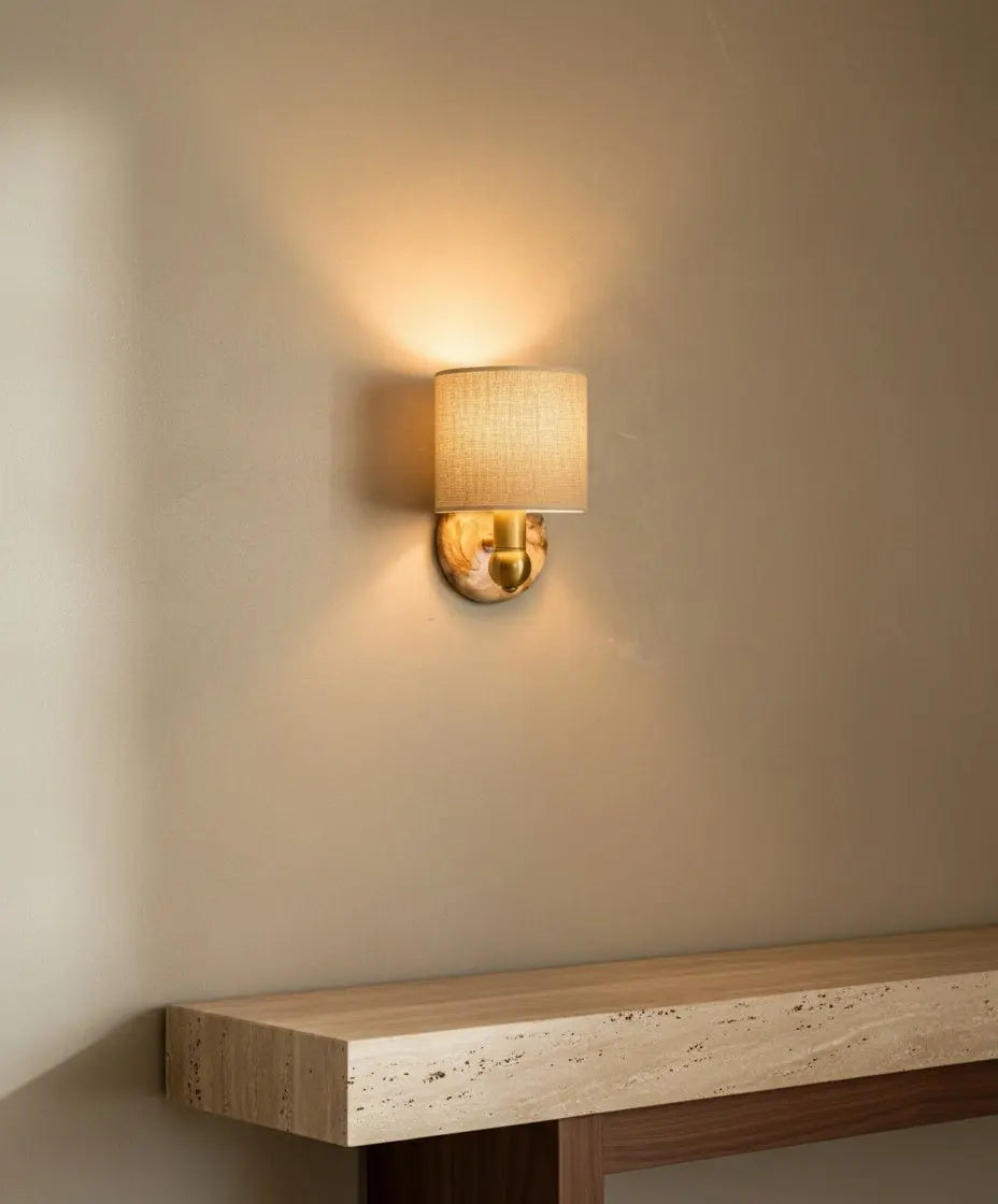 El aplique iluminado sobre una consola de travertino, proyectando una luz cálida y sombras suaves en forma de abanico.