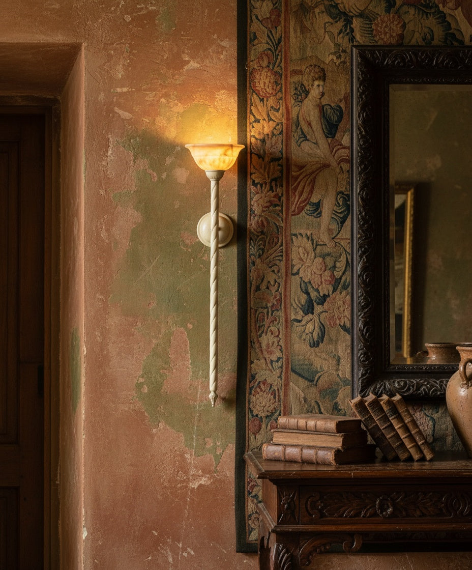 Aplique de pared antorcha encendido sobre una consola de madera rústica con libros antiguos y vasija de barro, luz cálida.