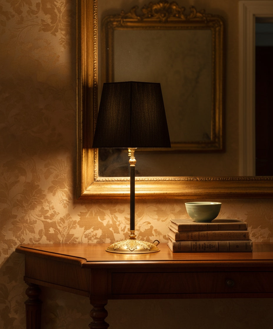 Primer plano de lámpara junto a libros antiguos y espejo dorado, destacando el relieve de la base.