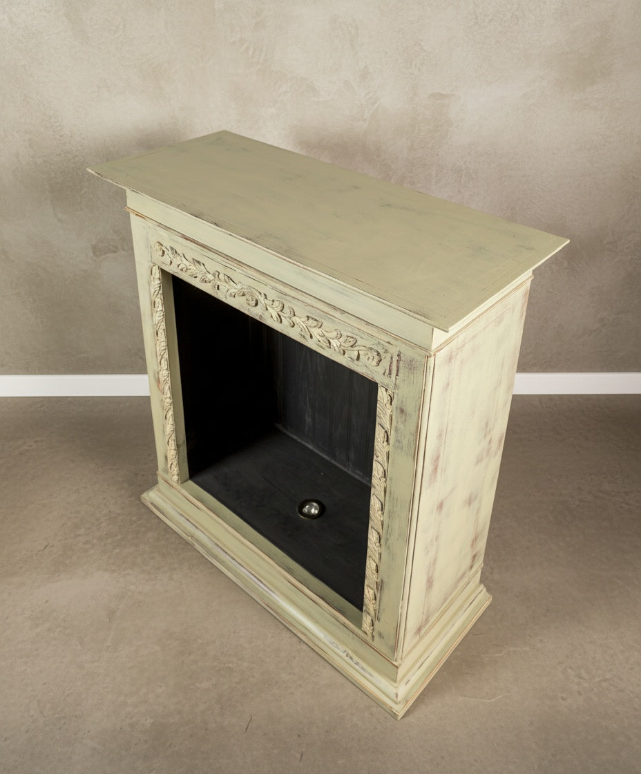 Vista superior de la chimenea decorativa verde pátina con talla floral sobre fondo neutro.