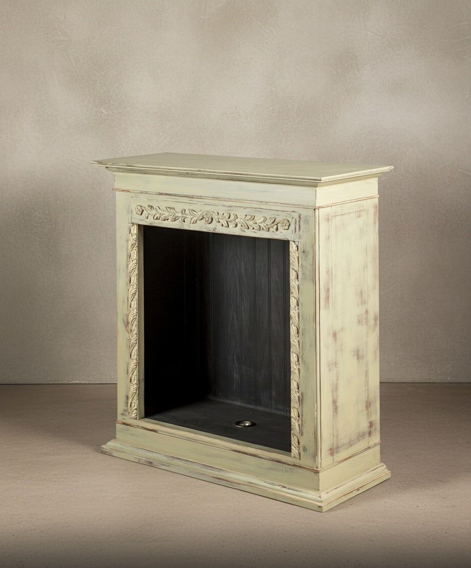 Vista lateral de la chimenea decorativa verde pátina con talla floral sobre fondo neutro.