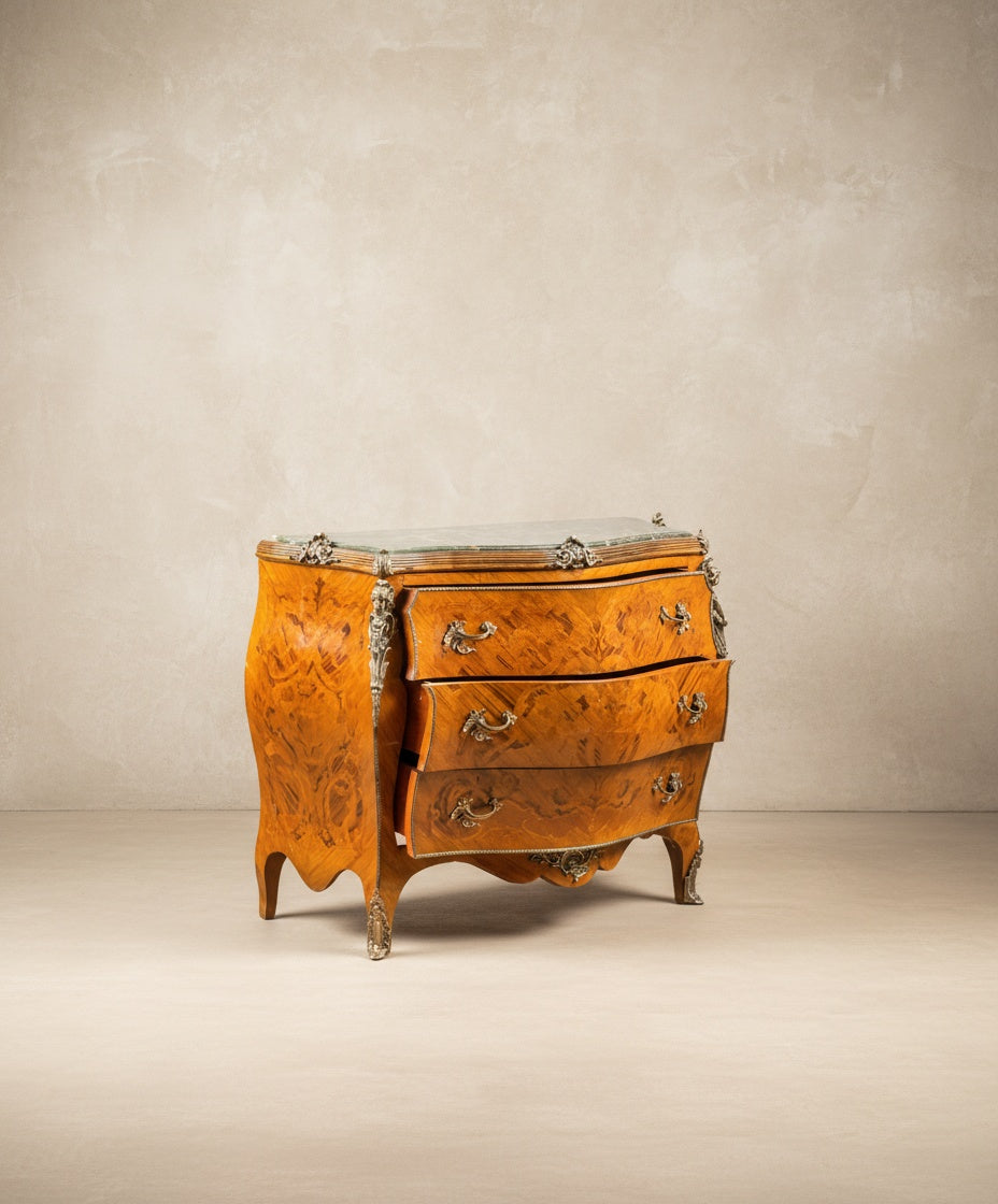 Vista angular de la cómoda resaltando la curvatura lateral y los herrajes de bronce cincelado.