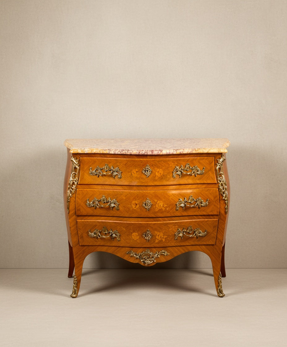 Vista frontal de cómoda estilo Luis XV con tres cajones y encimera de mármol veteado.