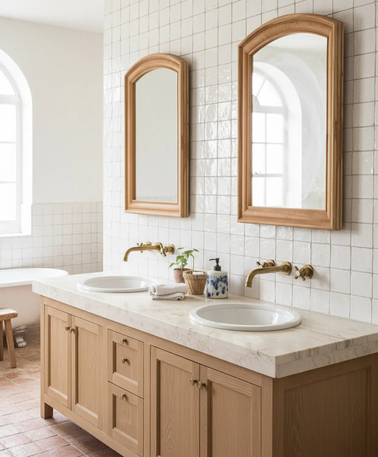 Dos espejos de madera arqueados colocados sobre lavabo doble en baño de estilo mediterráneo