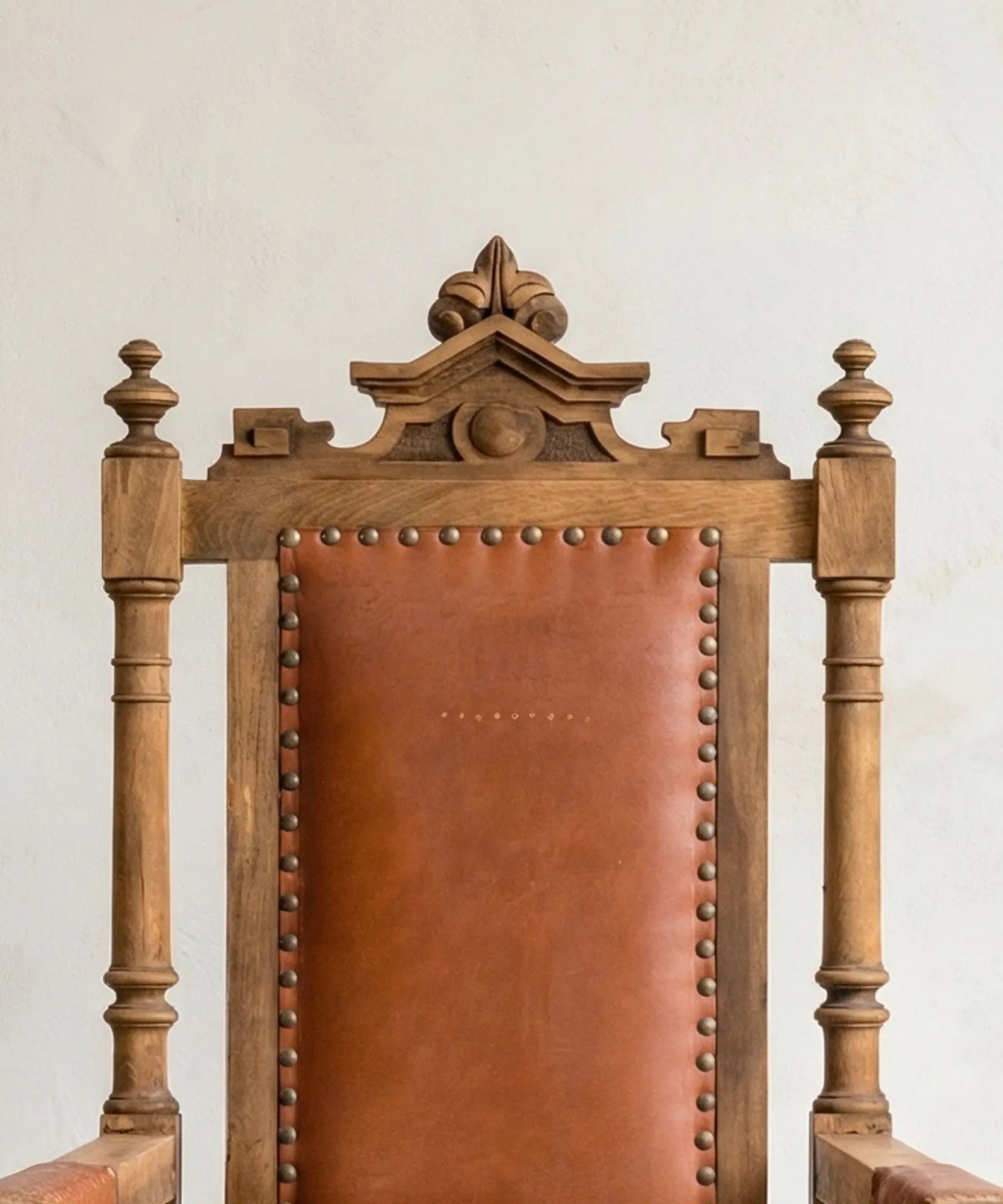 Respaldo de cuero y madera tallada con remates torneados en sillón de estilo renacentista.