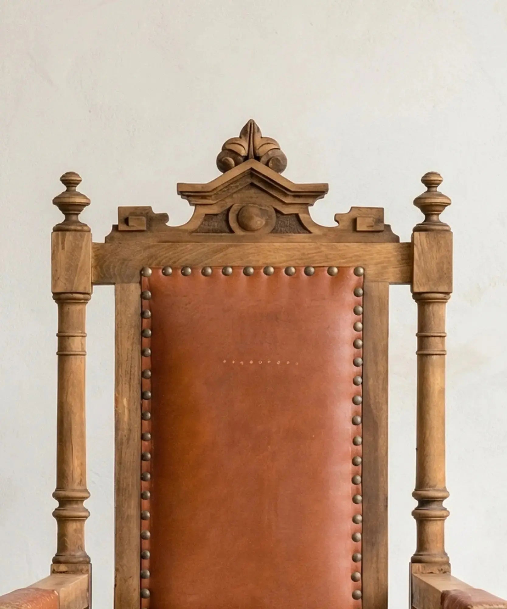 Respaldo de cuero y madera tallada con remates torneados en sillón de estilo renacentista.