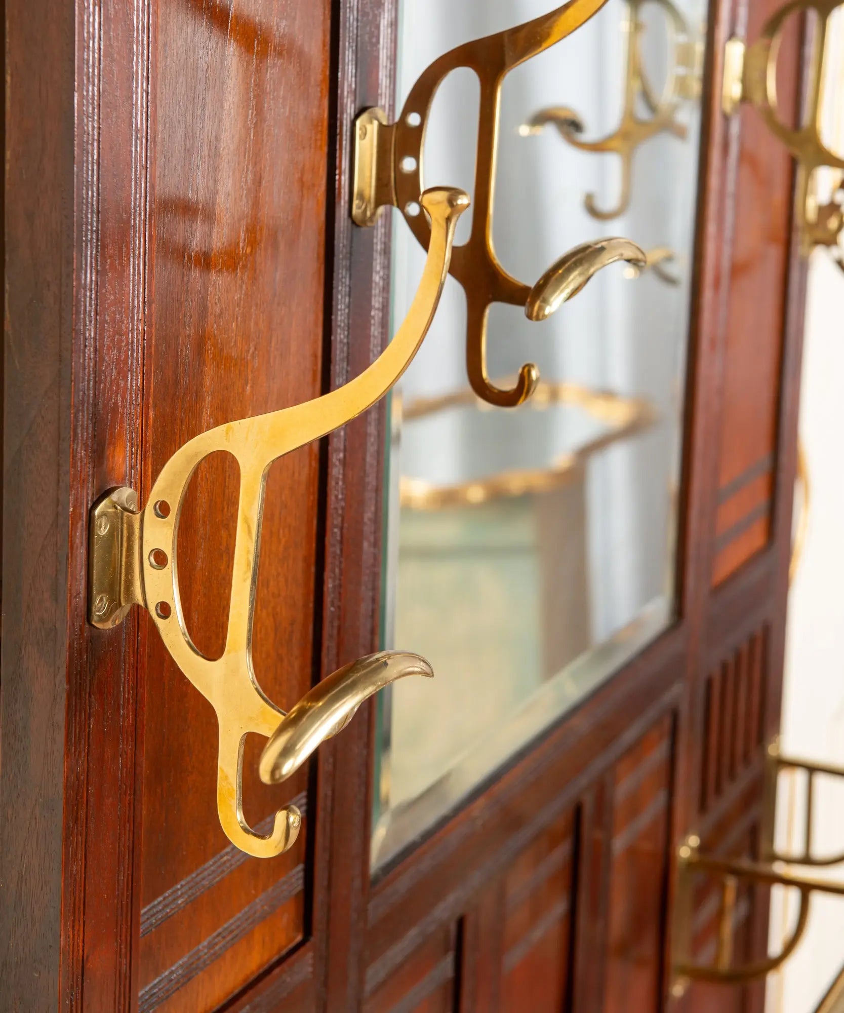 Primer plano de percha curva de bronce macizo pulido sobre madera de caoba antigua.