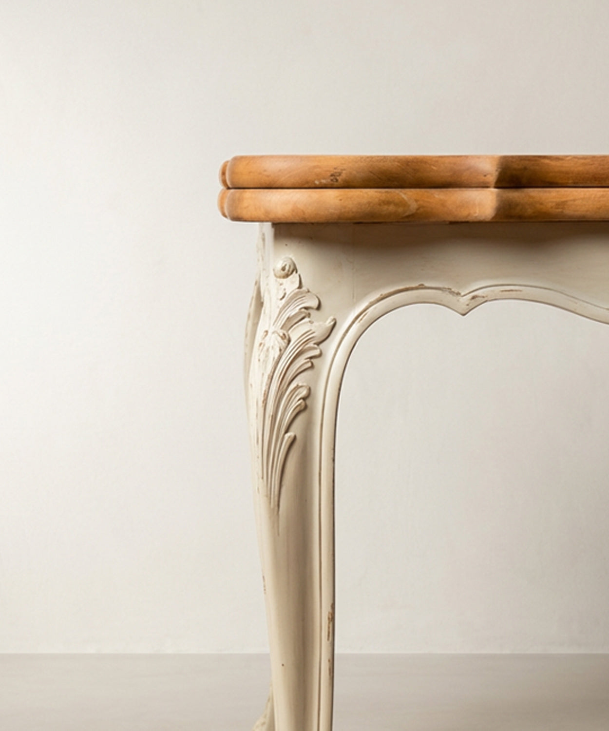 Primer plano del faldón tallado con motivo de concha y patas cabriolé en pátina crema.