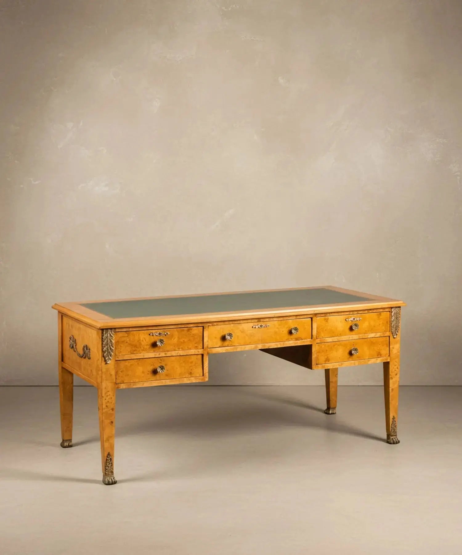 Escritorio estilo Imperio en madera de raíz con cinco cajones y tapete de piel verde frontal.