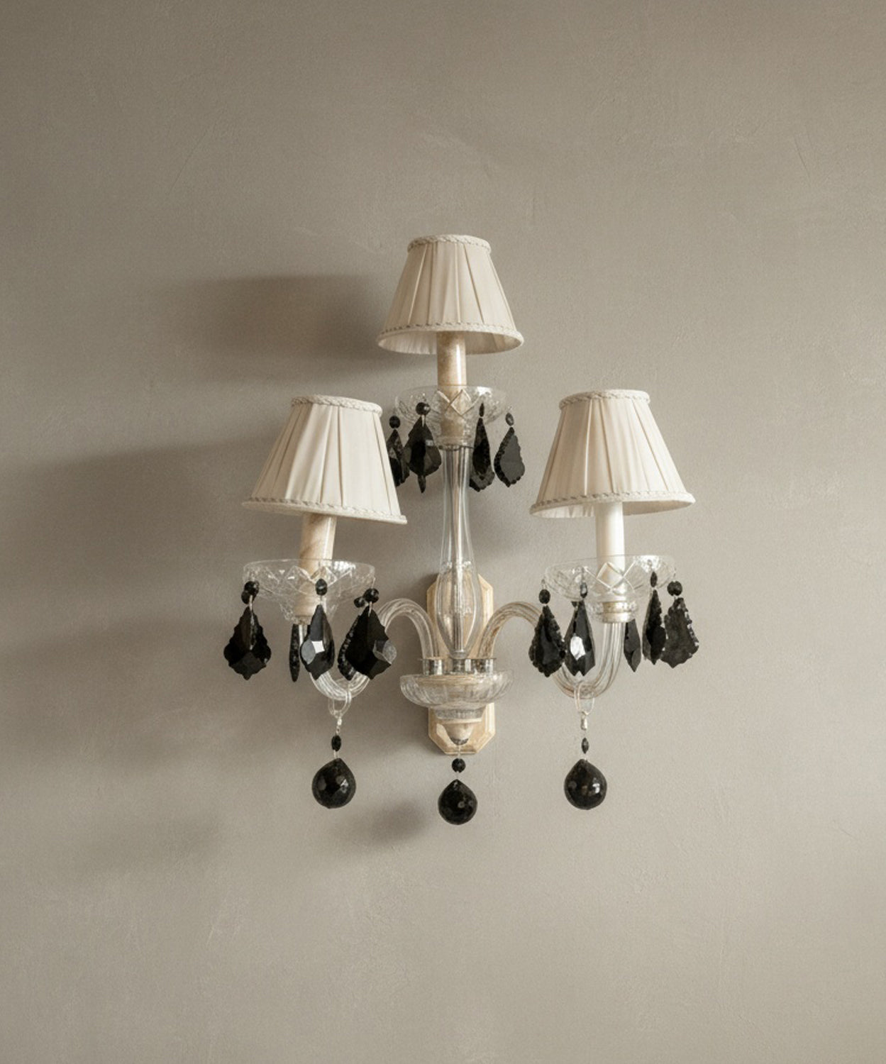 Aplique de pared vintage de 3 luces con brazos de cristal y lágrimas negras colgantes sobre pared beige.