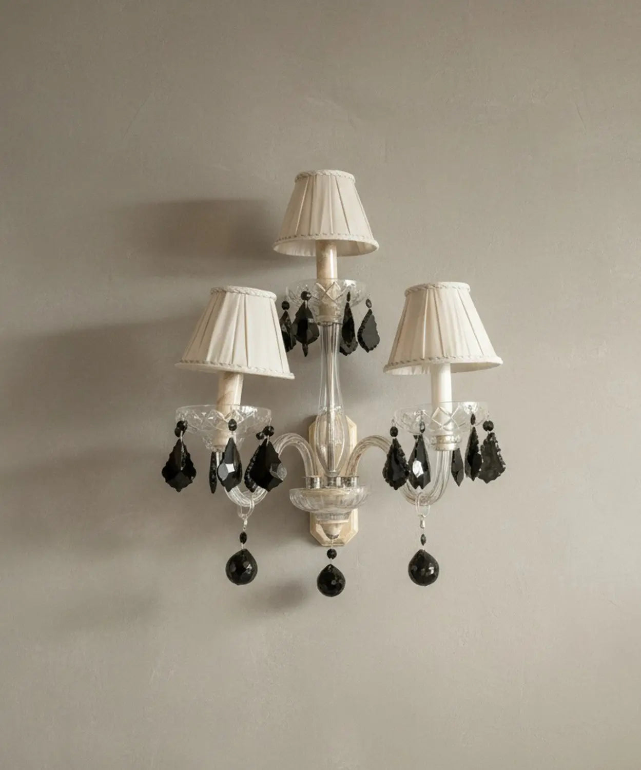 Aplique de pared vintage de 3 luces con brazos de cristal y lágrimas negras colgantes sobre pared beige.