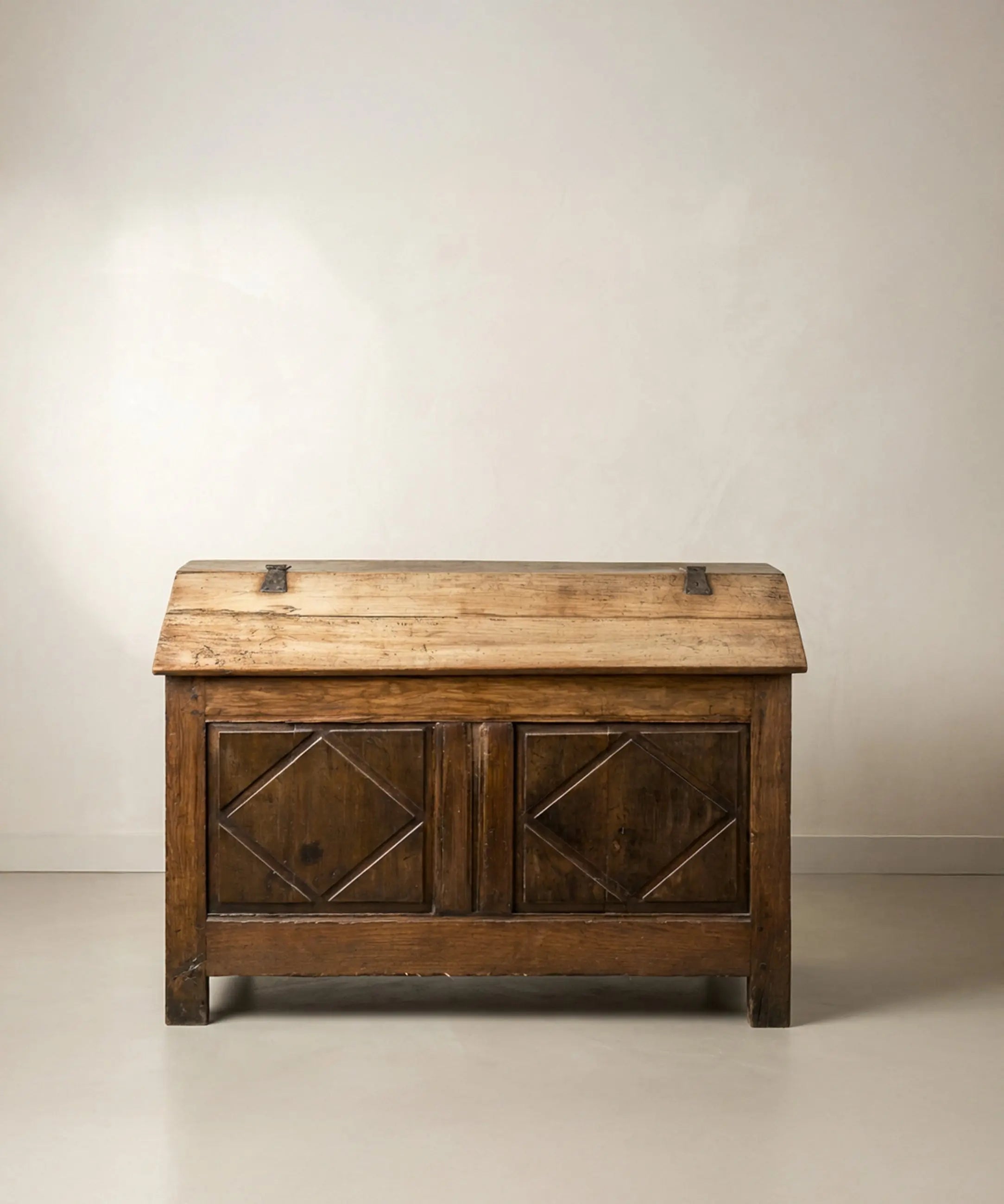 Vista frontal de arca antigua de madera con tapa inclinada y tallas de rombos.