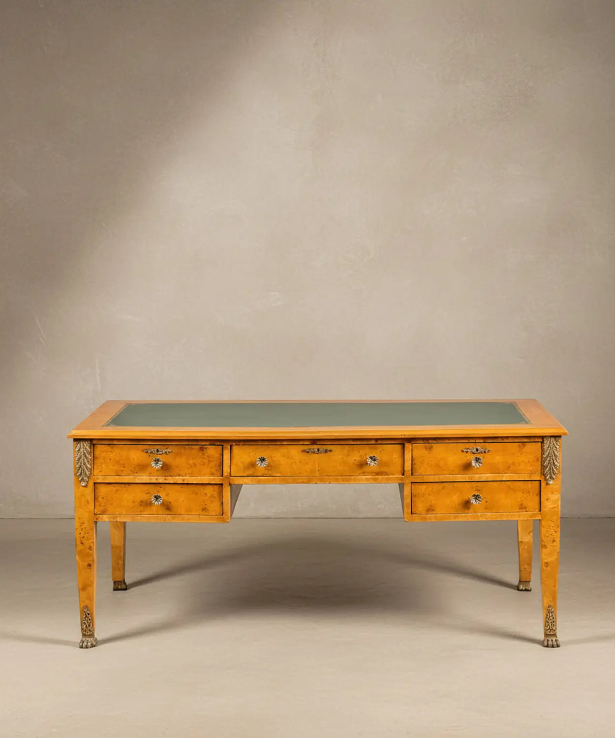 Escritorio estilo Imperio en madera de raíz con cinco cajones y tapete de piel verde frontal.