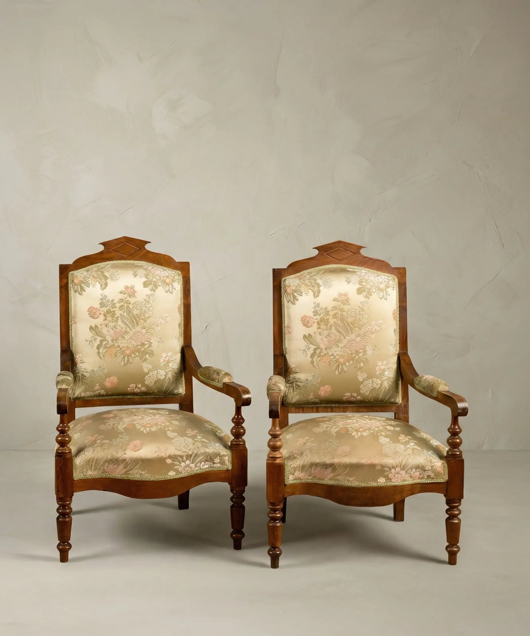 Pareja de sillones antiguos estilo neoclásico con tapicería floral sobre fondo de papel pintado paisajístico sepia.