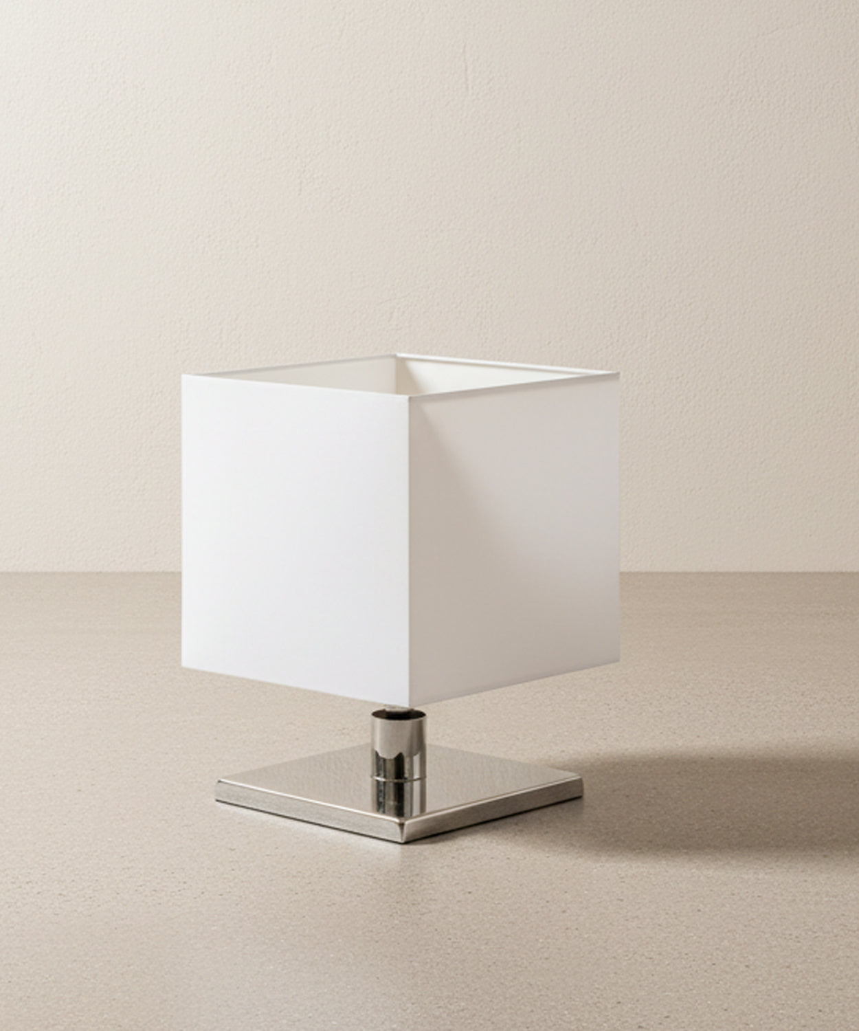 Detalle en ángulo de lámpara moderna resaltando el acabado espejo de la base metálica cuadrada.