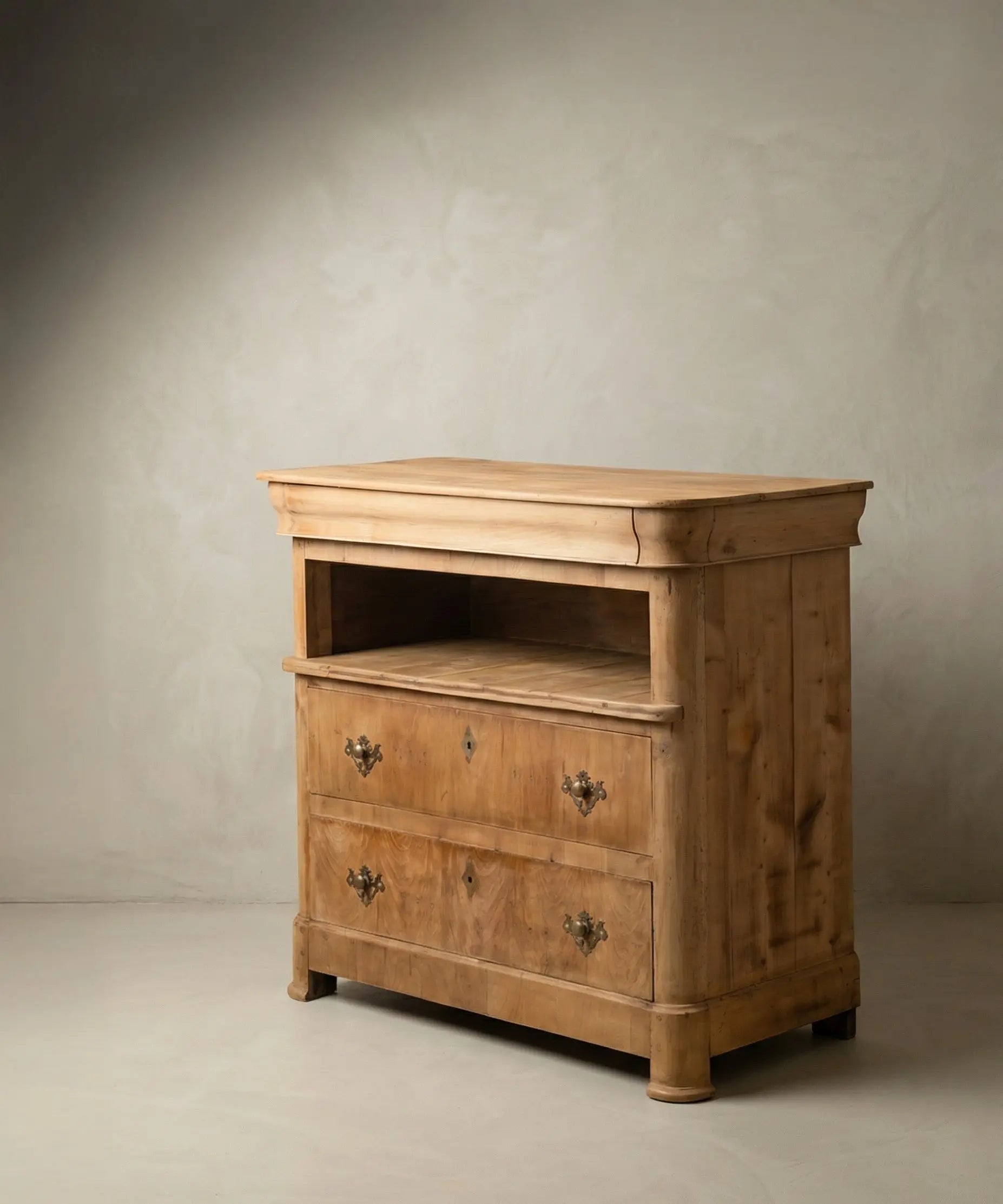 Cómoda antigua de madera clara mostrando el cajón superior oculto en gola y herrajes de bronce.