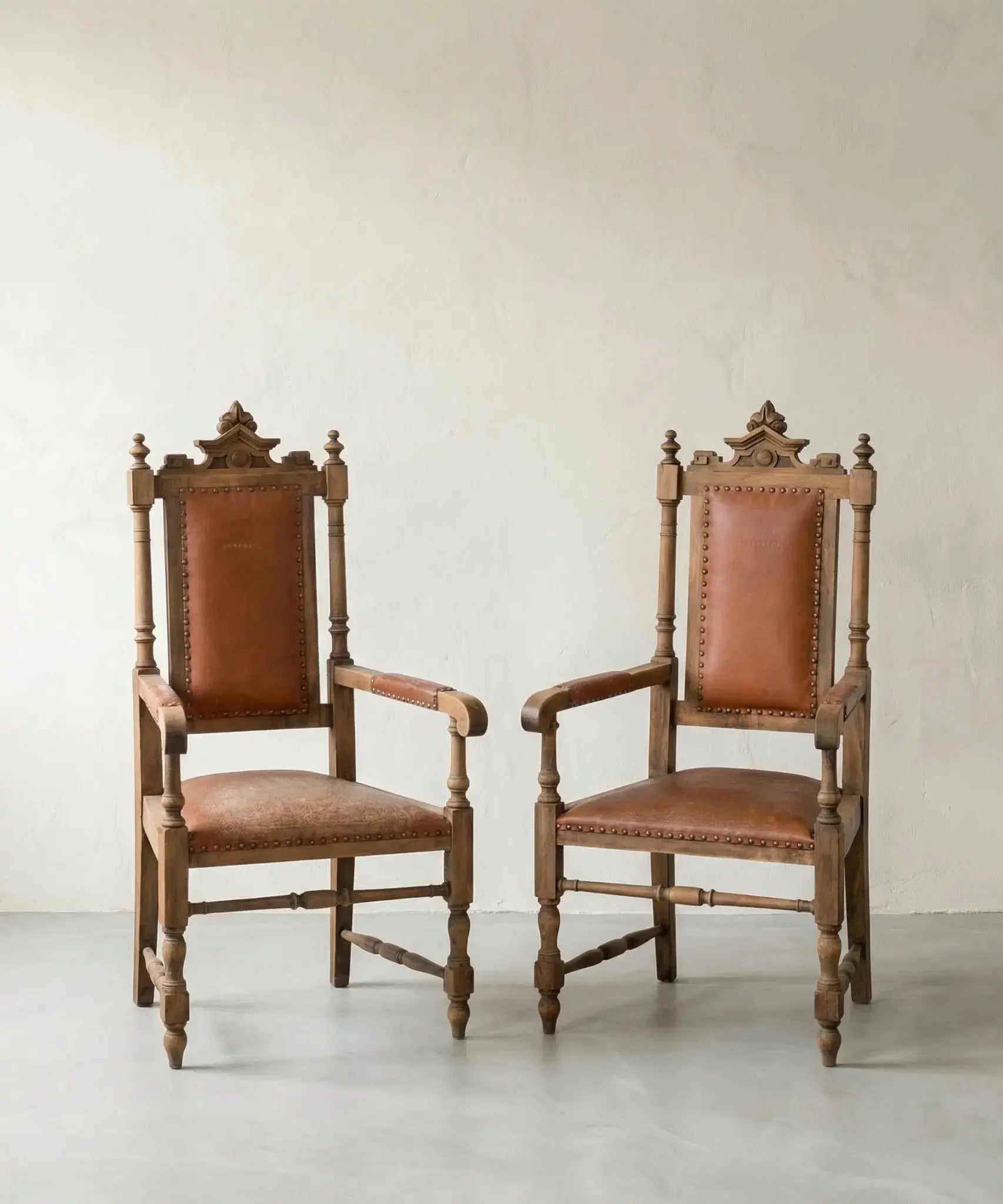 Pareja de sillones fraileros clásicos de madera y cuero marrón con tachuelas.