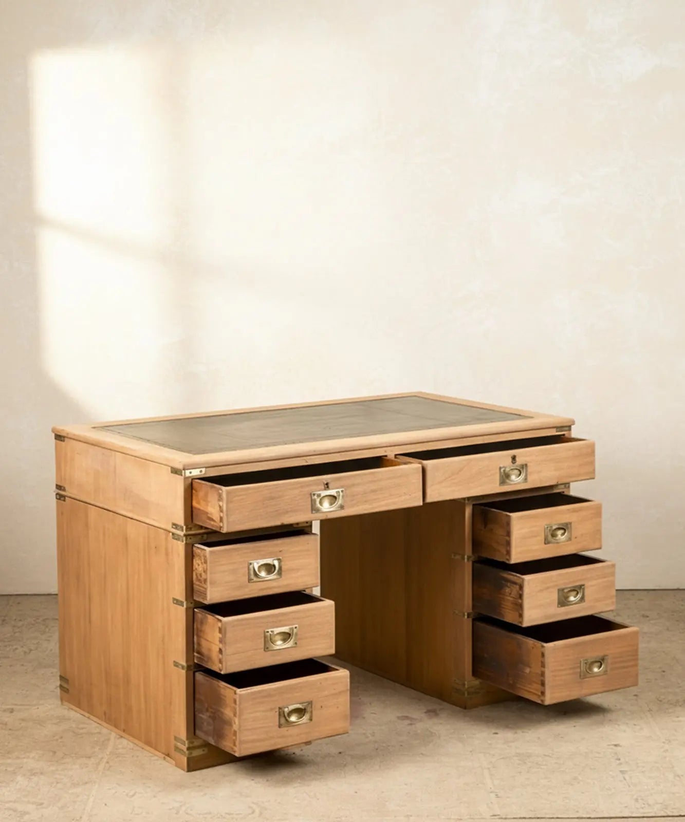 Escritorio de campaña inglés de madera clara con ocho cajones y sobre de cuero verde en ambiente de estudio.