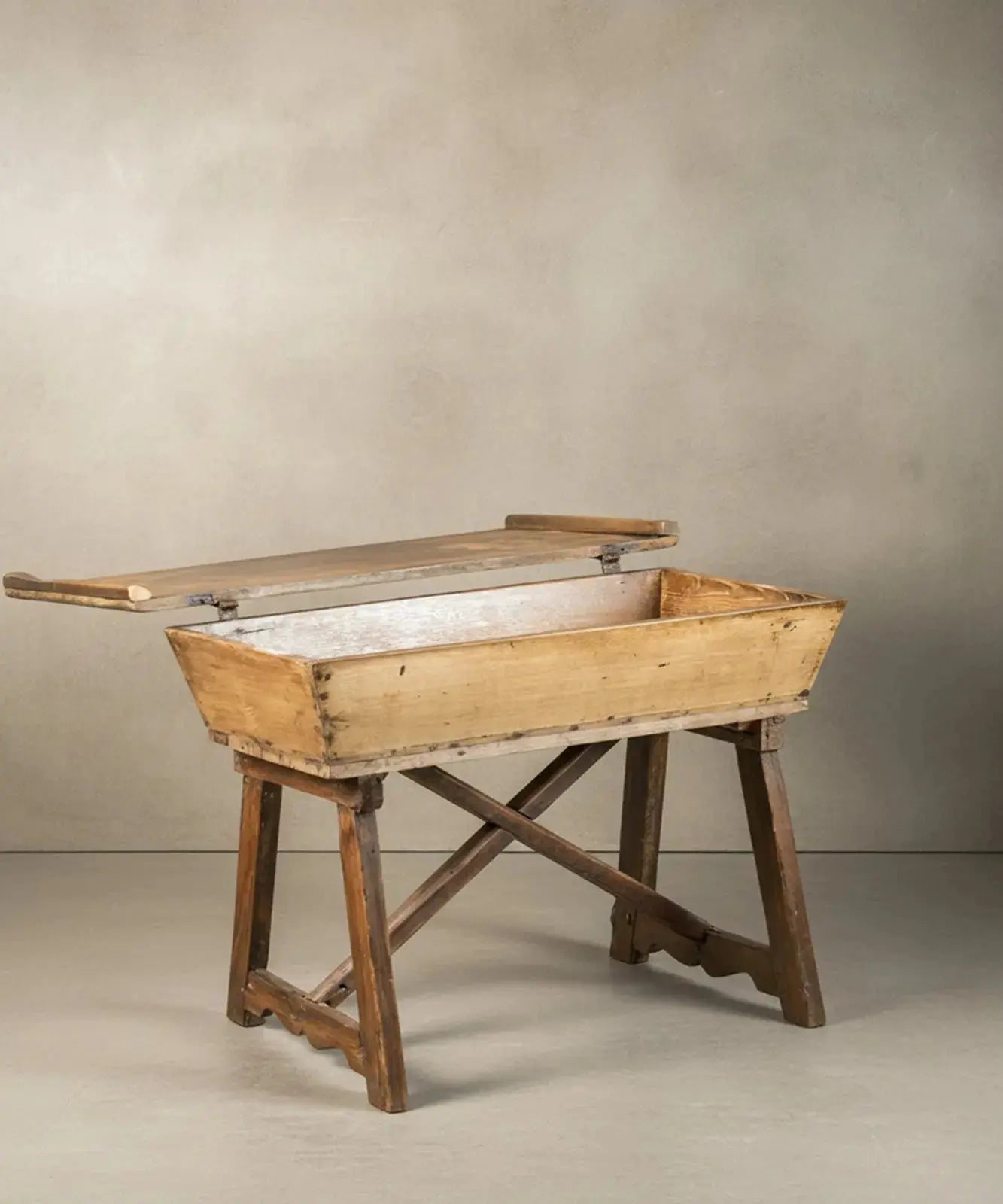 Mesa artesa antigua de madera maciza con tapa cerrada sobre fondo neutro, estilo rústico.