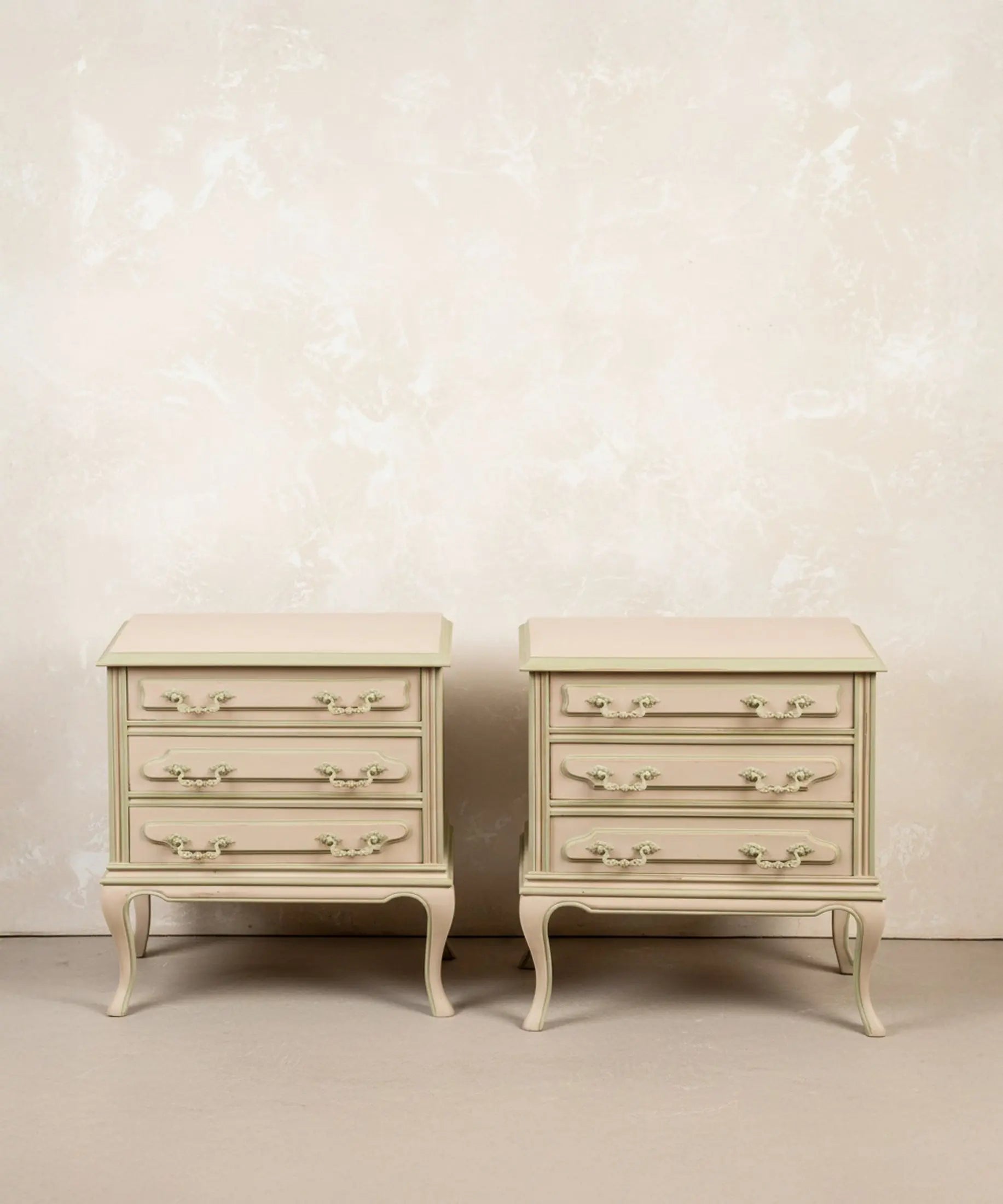 Pareja de mesitas de noche vintage de tres cajones pintadas en beige y verde salvia con patas curvas.