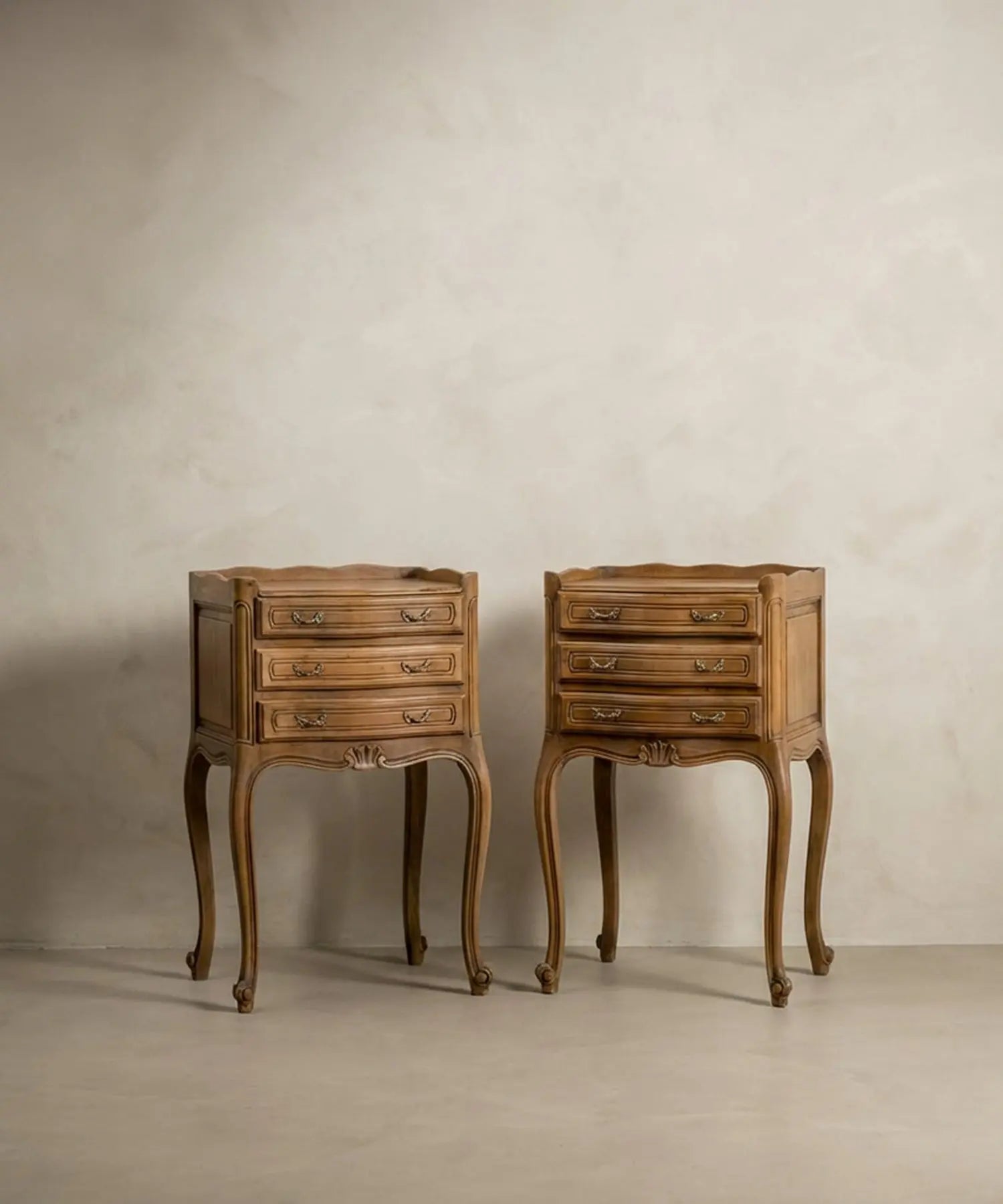 Vista frontal de pareja de mesitas de noche estilo Luis XV en madera natural clara sobre fondo neutro.