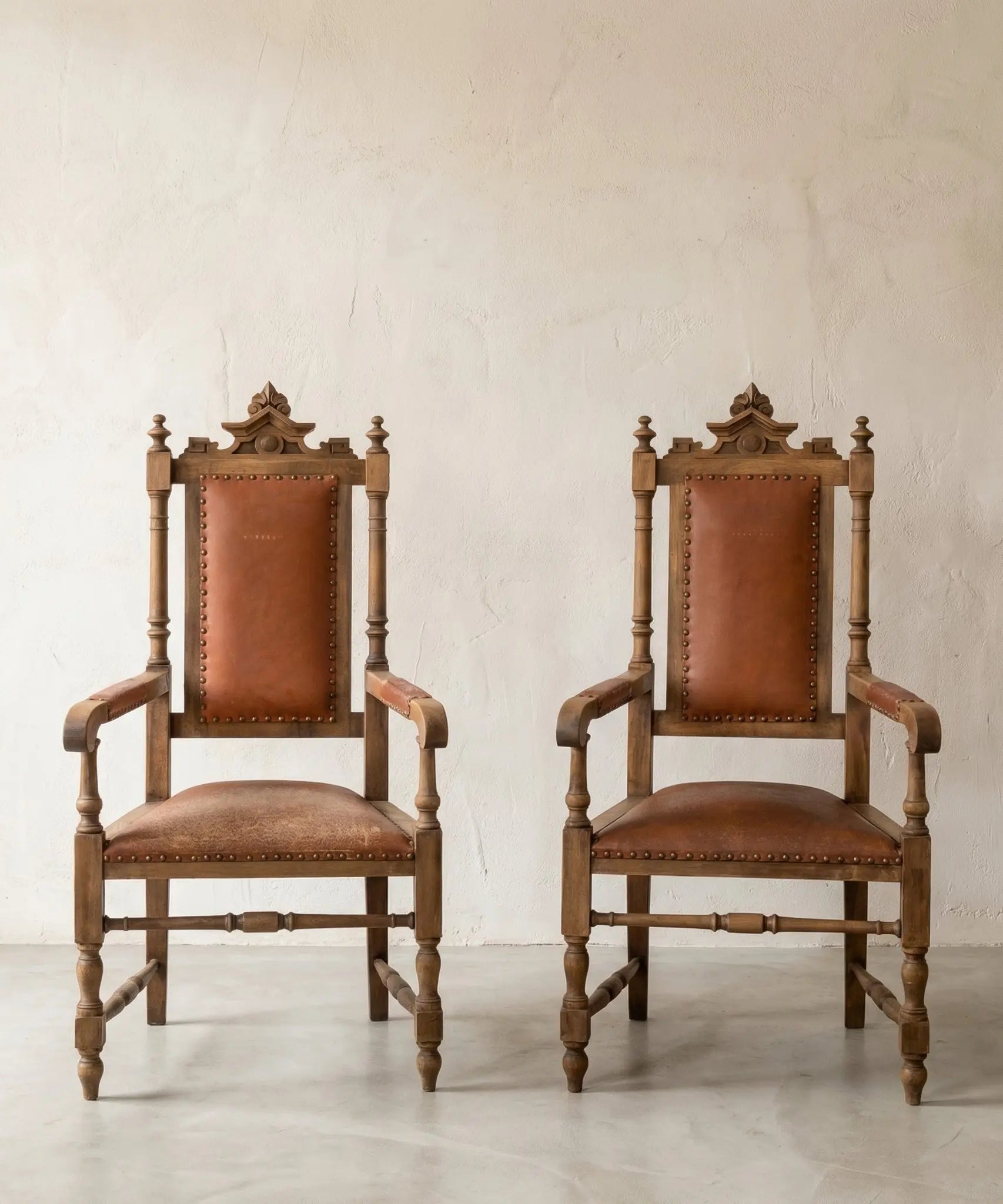 Pareja de sillones fraileros clásicos de madera y cuero marrón con tachuelas.