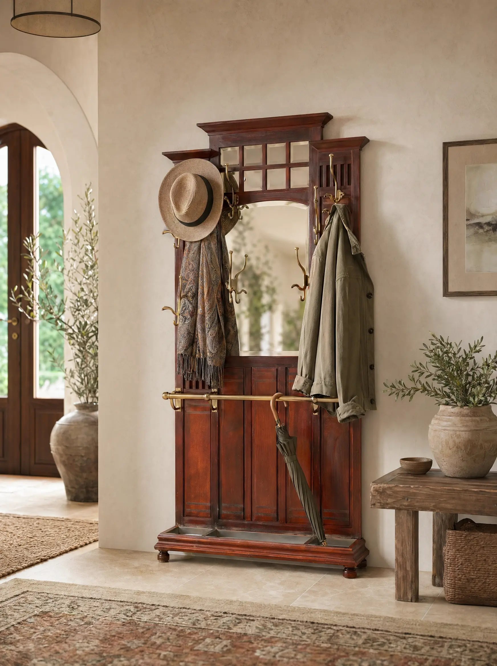Mueble recibidor antiguo de madera de caoba con espejo central y colgadores de bronce decorando una entrada de casa de estilo mediterraneo