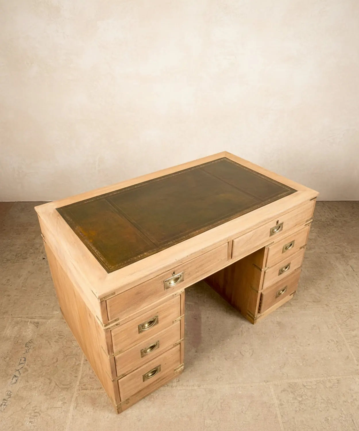 Escritorio de campaña inglés de madera clara con ocho cajones y sobre de cuero verde en ambiente de estudio.