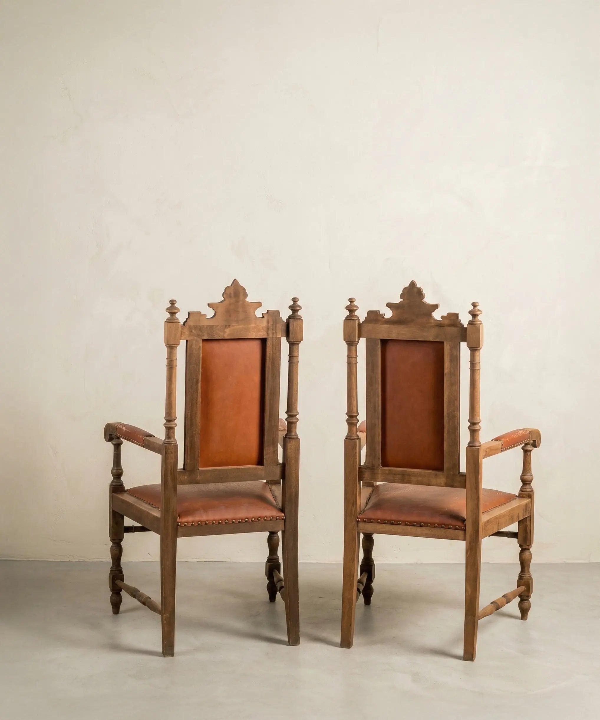 Vista lateral de dos sillas con brazos de madera maciza torneada y tapicería de piel vintage.