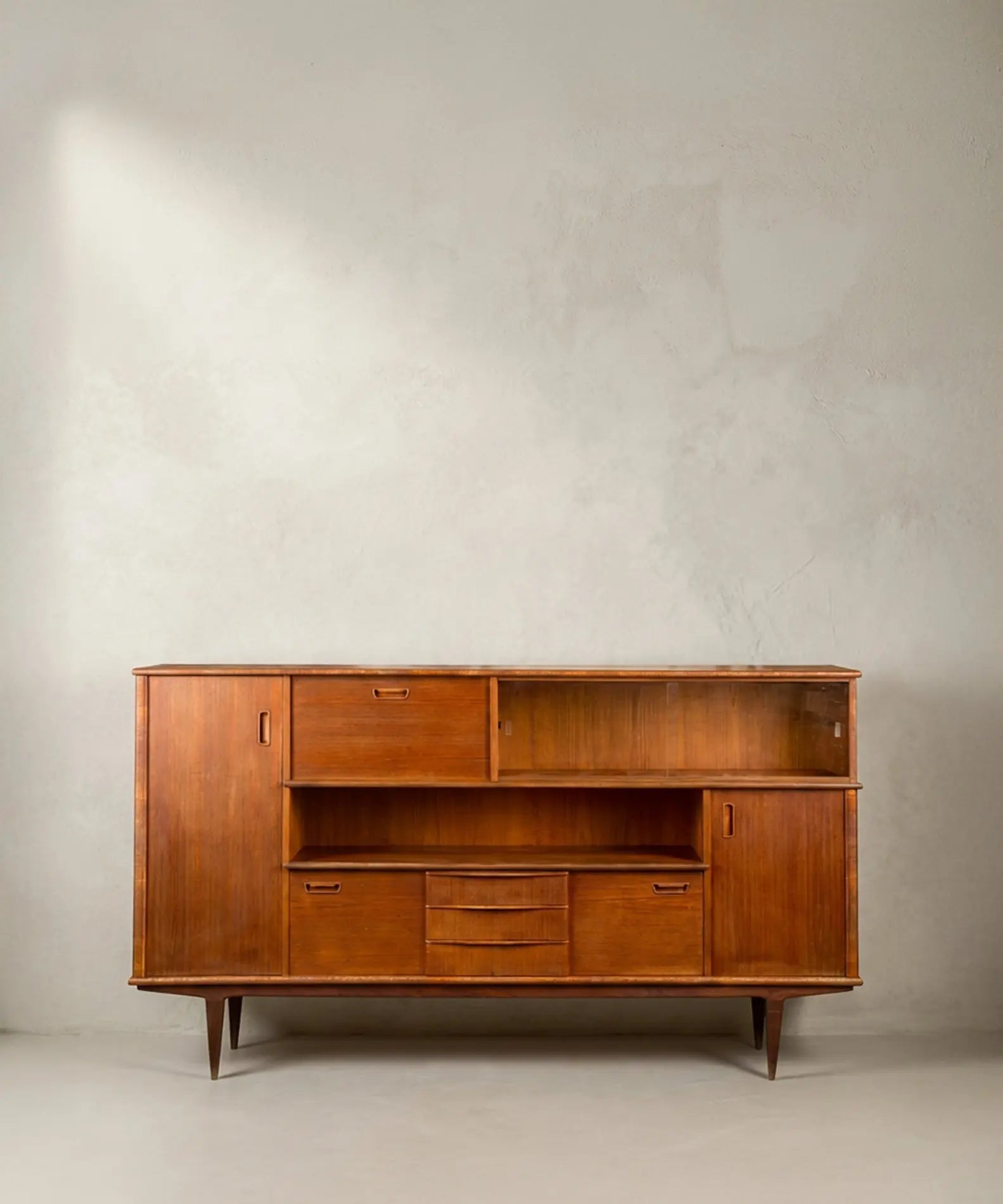 Aparador Mid-Century Modern de teca con puertas y vitrina frontal sobre fondo neutro.