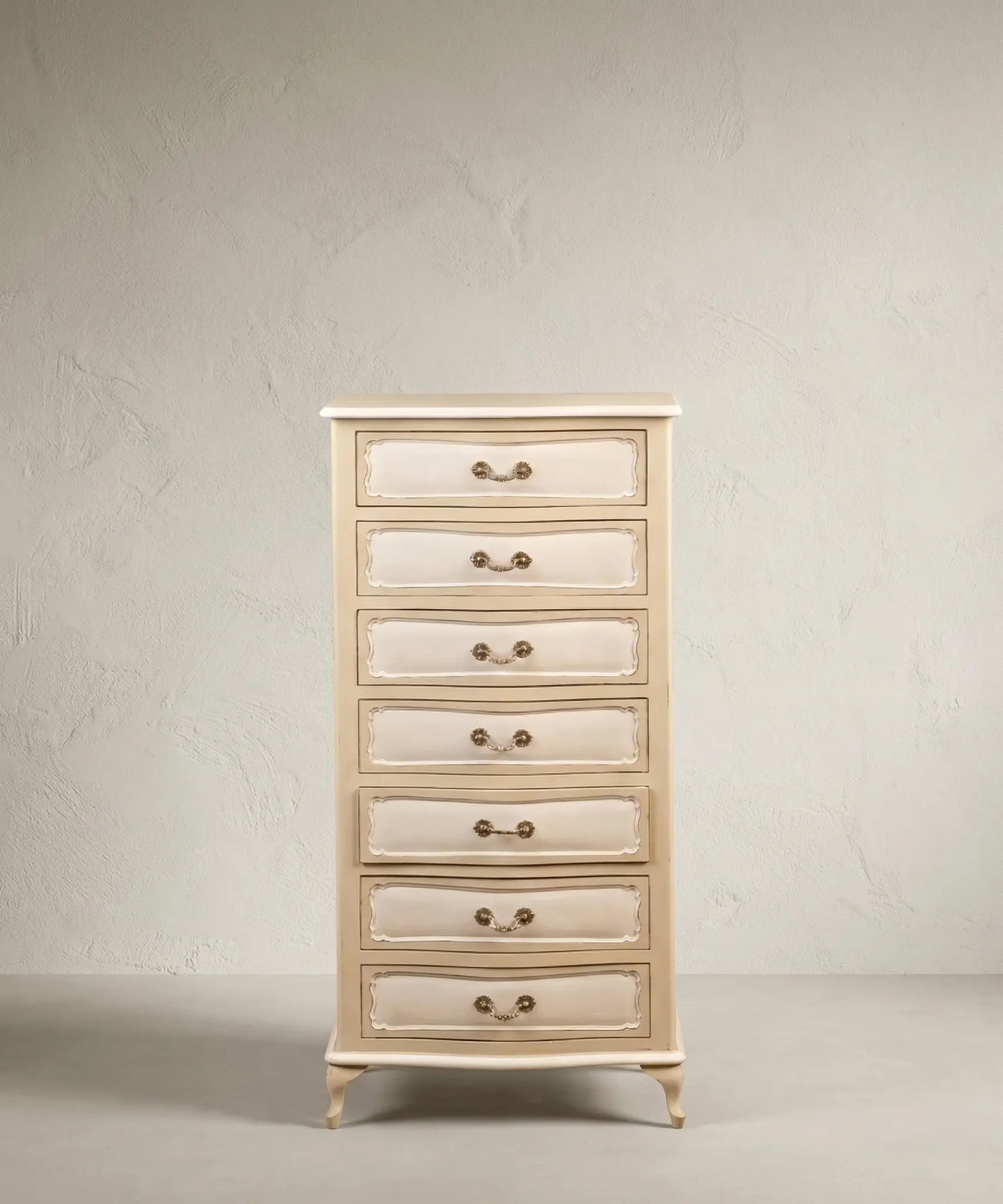 Semanier francés de 7 cajones en color crema y blanco, vista tres cuartos mostrando molduras y patas cabriolé sobre fondo neutro.