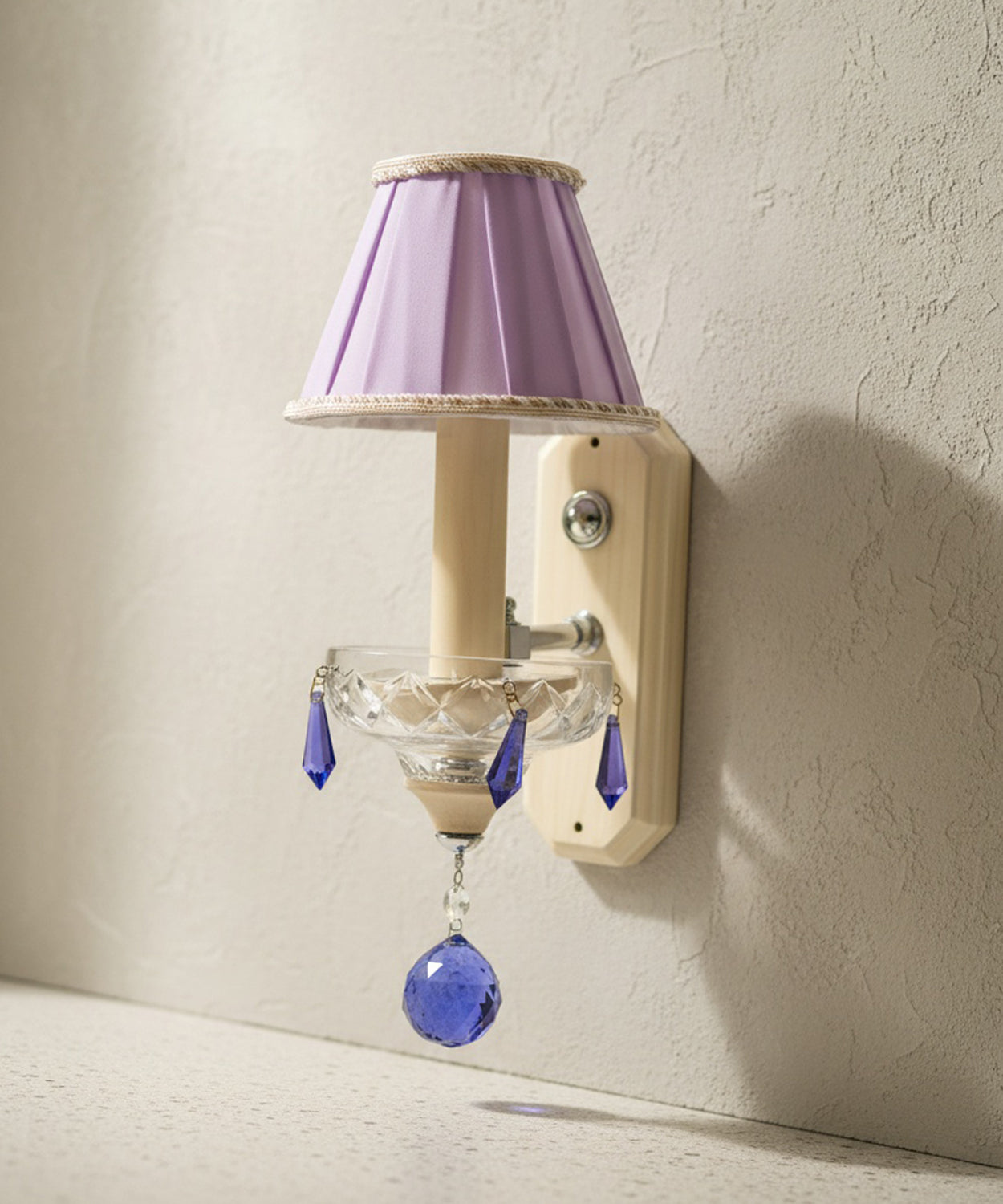 Detalle del soporte de pared en color crema y la bobeche de cristal facetado con colgantes azul cobalto.