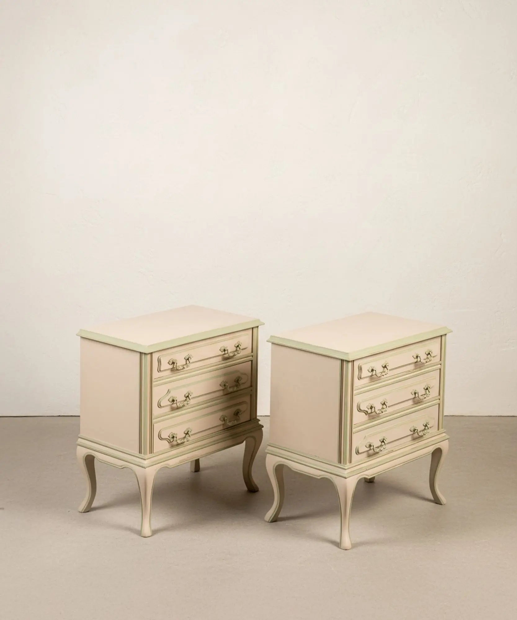 Pareja de mesitas de noche vintage de tres cajones pintadas en beige y verde salvia con patas curvas.