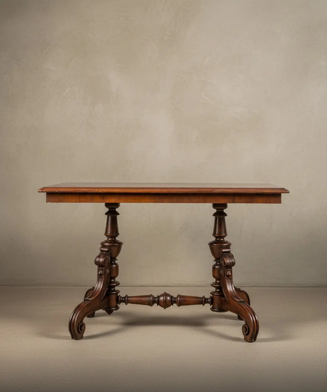 Mesa de centro victoriana en madera noble con base tallada y travesaño torneado sobre fondo neutro.