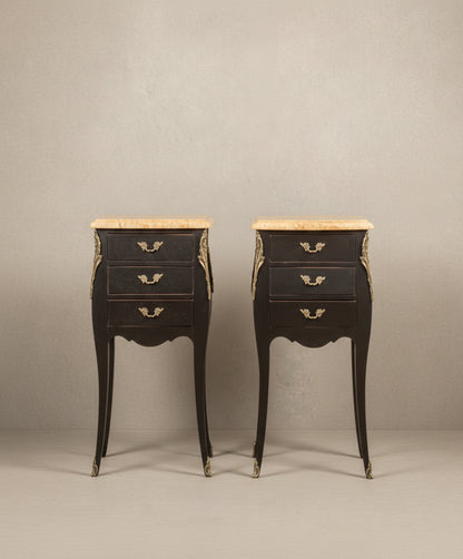 Pareja de mesillas de noche francesas estilo Luis XV en color negro mate con tres cajones y sobres de mármol.