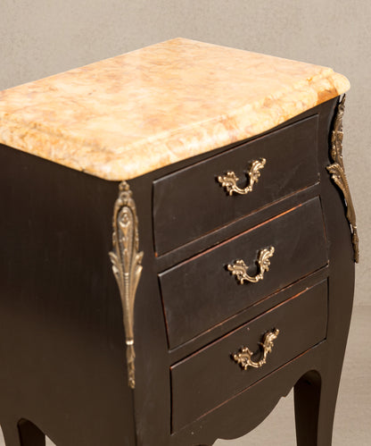 Primer plano del sobre de mármol veteado ámbar y tiradores de bronce cincelado sobre madera negra.