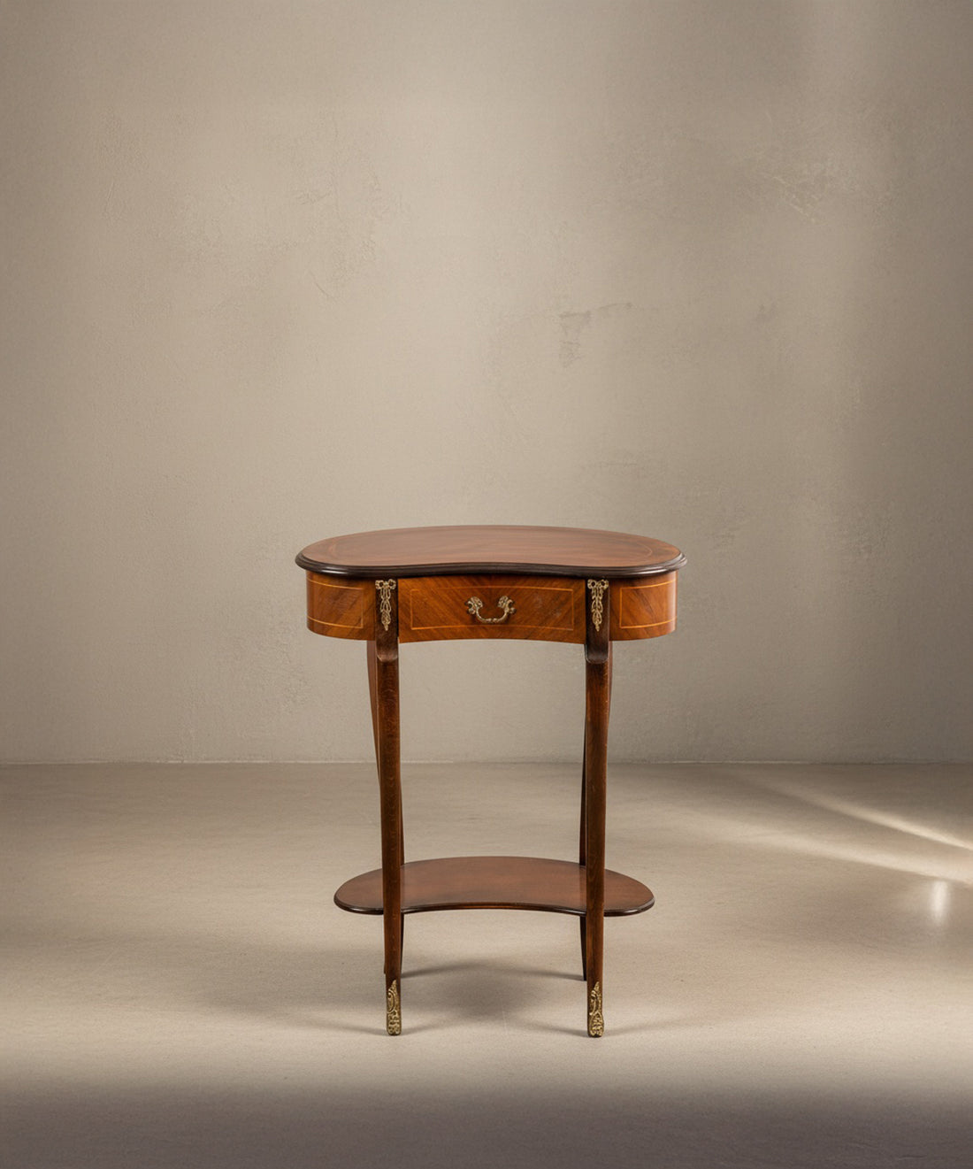 Vista frontal de mesa estilo Luis XV con bronces dorados y cajón central sobre fondo neutro.