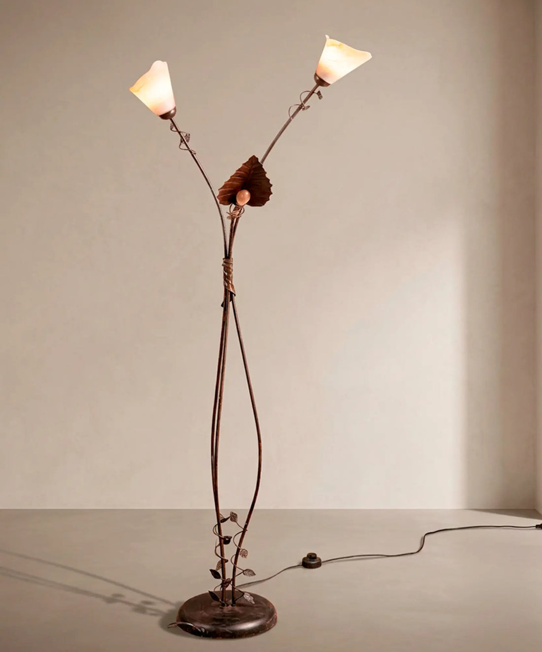 Lámpara de pie escultórica de hierro forjado con tres luces y tulipas de cristal ámbar encendidas.
