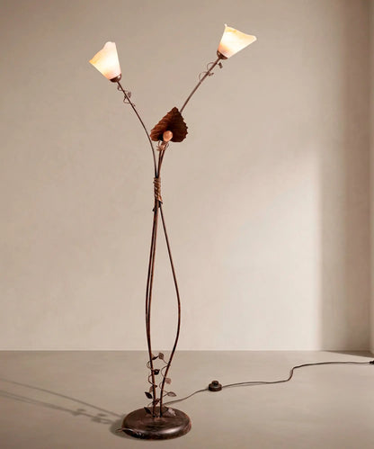 Lámpara de pie escultórica de hierro forjado con tres luces y tulipas de cristal ámbar encendidas.