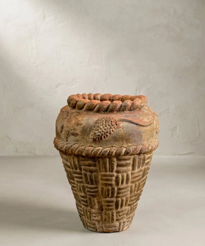 Gran macetero antiguo de terracota texturizada sobre fondo neutro.