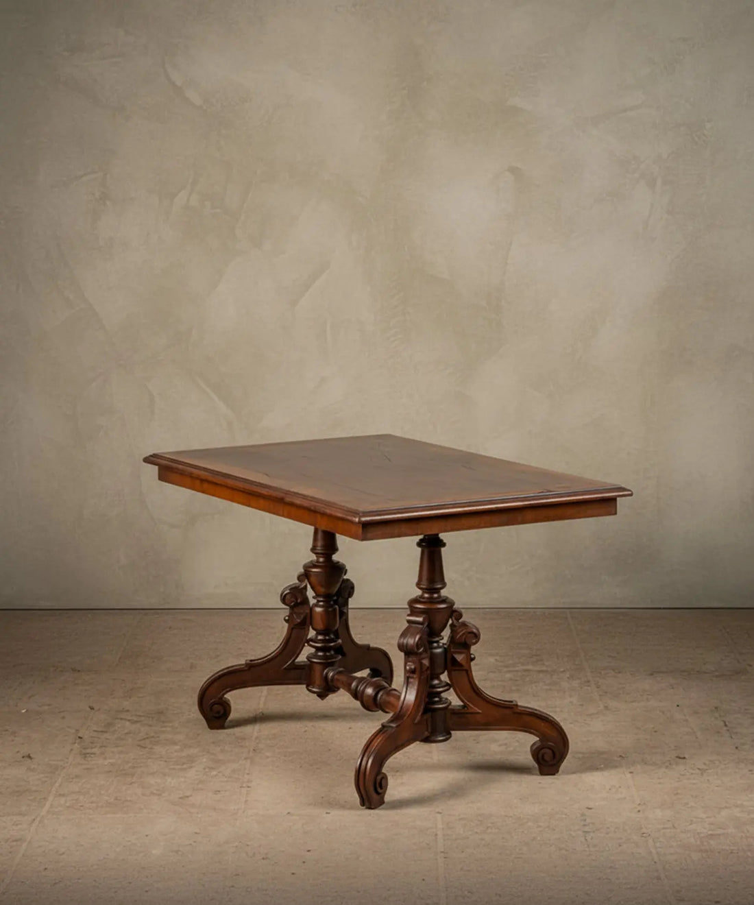 Mesa de centro victoriana en madera noble con base tallada y travesaño torneado sobre fondo neutro.