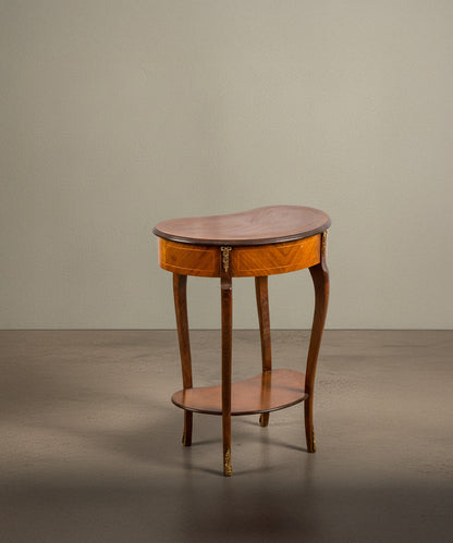 Vista trasera de mesa estilo Luis XV con bronces dorados y cajón central sobre fondo neutro.